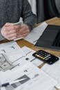 Hands counting money at a workspace with a laptop, calculator, and financial documents.