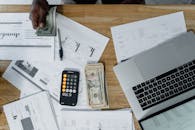 Overhead view of a busy workspace with cash, financial documents, and a laptop.