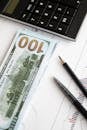 Stack of hundred dollar bills beside calculator and graph for financial analysis